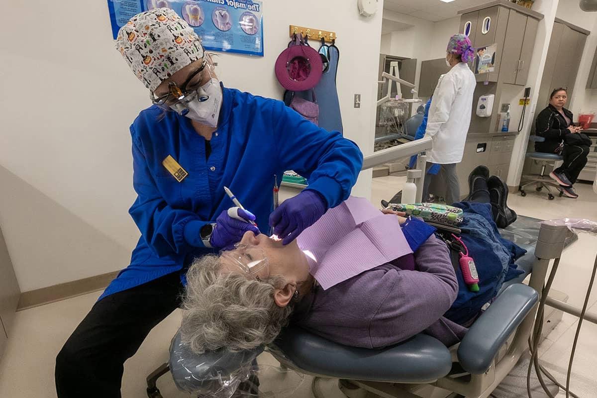 A student hygienist examines the mouth of a woman laying in a dental chair